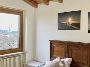 A room with a wooden headboard, a radiator, a small bedside table, and a window with a view of a cityscape.