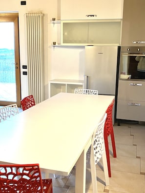 A compact kitchen with a dining area, a refrigerator, and a window with curtains.