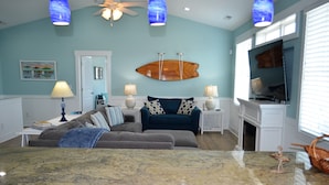 A living room with a blue couch, a coffee table, and a television. There is a ceiling fan, a wall-mounted fish decoration, and a fireplace. - Ohana - Walk to beach in Surfside Beach (Surfside Beach)