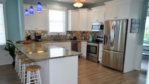 A modern kitchen with white cabinets, a stainless steel refrigerator, a built-in oven, and a large island with bar stools. - Ohana - Walk to beach in Surfside Beach (Surfside Beach)