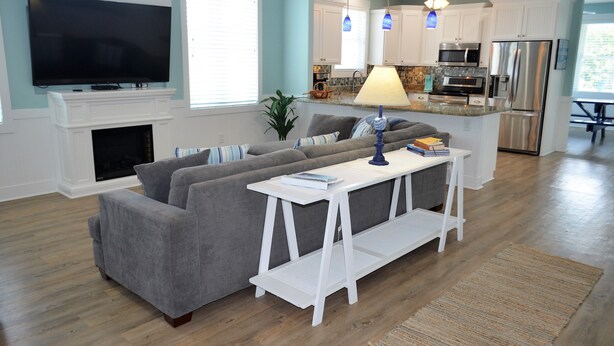 A modern living room with a grey sofa, a white coffee table, and a flat-screen TV above a fireplace. - Ohana - Walk to beach in Surfside Beach (Surfside Beach)