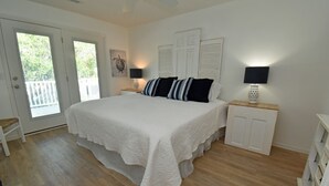 A bedroom with a large bed, two bedside tables with lamps, a door, and a view of the outdoors. - Windjammer - Walk to Beach in Garden City Beach (Garden City)
