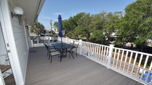 A wooden deck with a table and chairs, a white railing, and trees in the background. - Windjammer - Walk to Beach in Garden City Beach (Garden City)