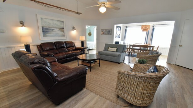 A living room with a brown leather sofa, a grey sofa, a wicker chair, and a dining table with chairs. - Windjammer - Walk to Beach in Garden City Beach (Garden City)