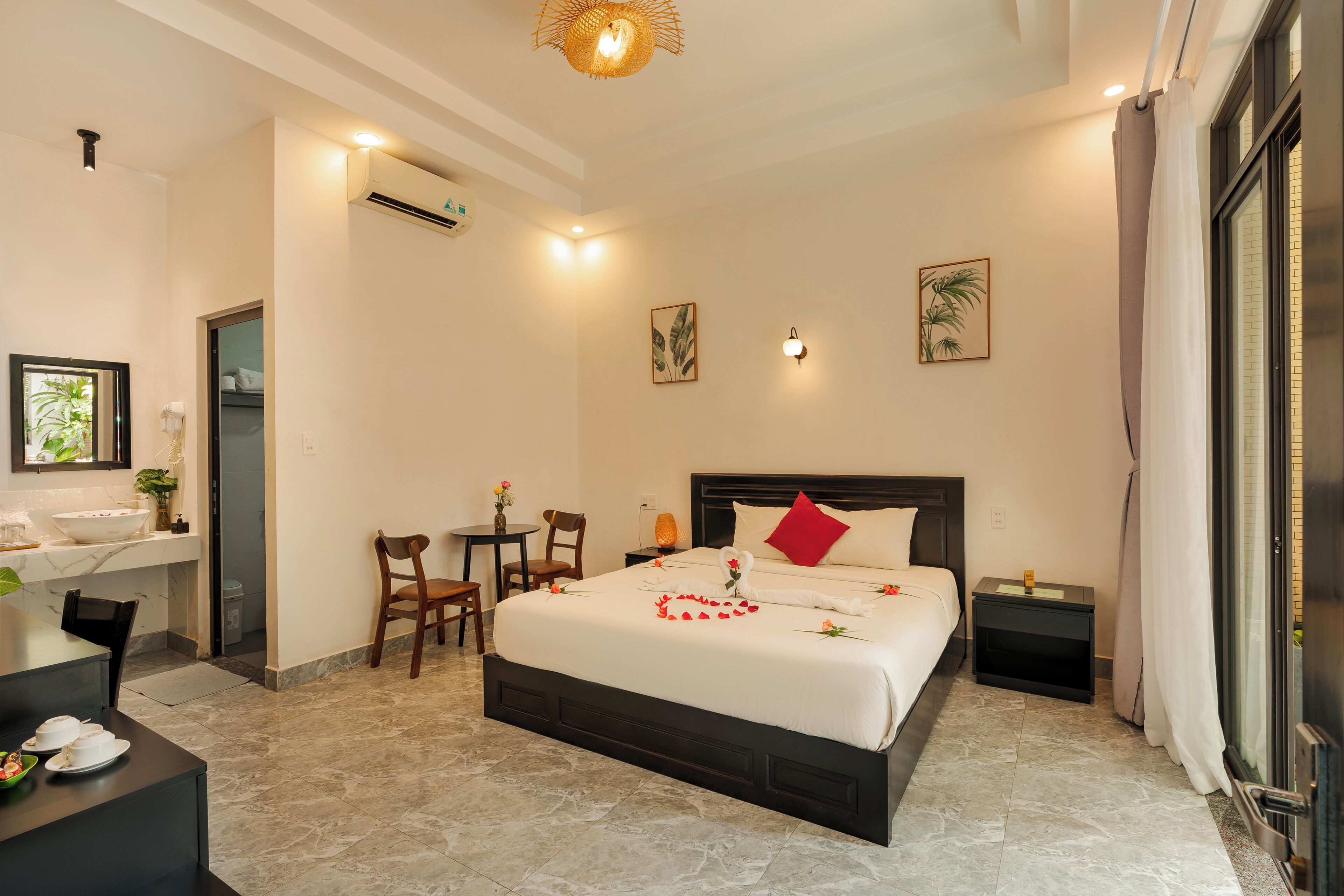 A hotel room with a bed, bedside table, chair, desk, and a bathroom with a sink and mirror.