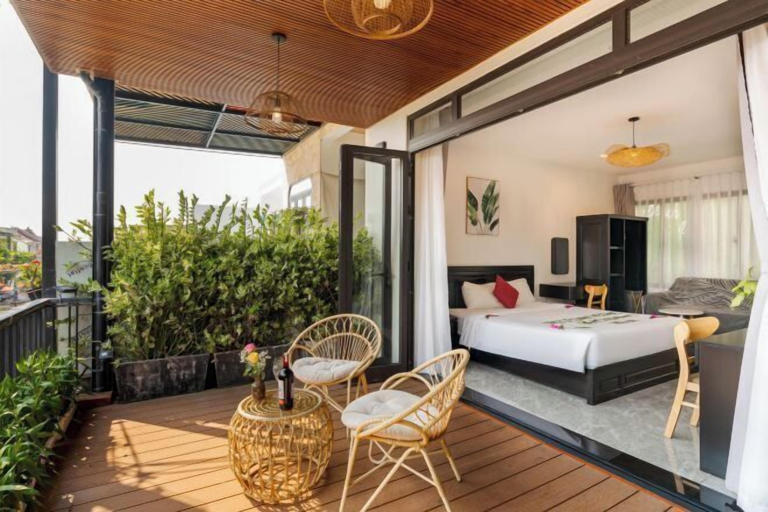 A modern bedroom with a large bed, a small seating area, and a balcony with plants.