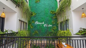 Un balcón con pared verde, plantas en macetas y una mesa de madera.