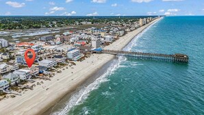 Une vue aérienne d’une ville côtière, avec une plage, une jetée et un ensemble dense de bâtiments.