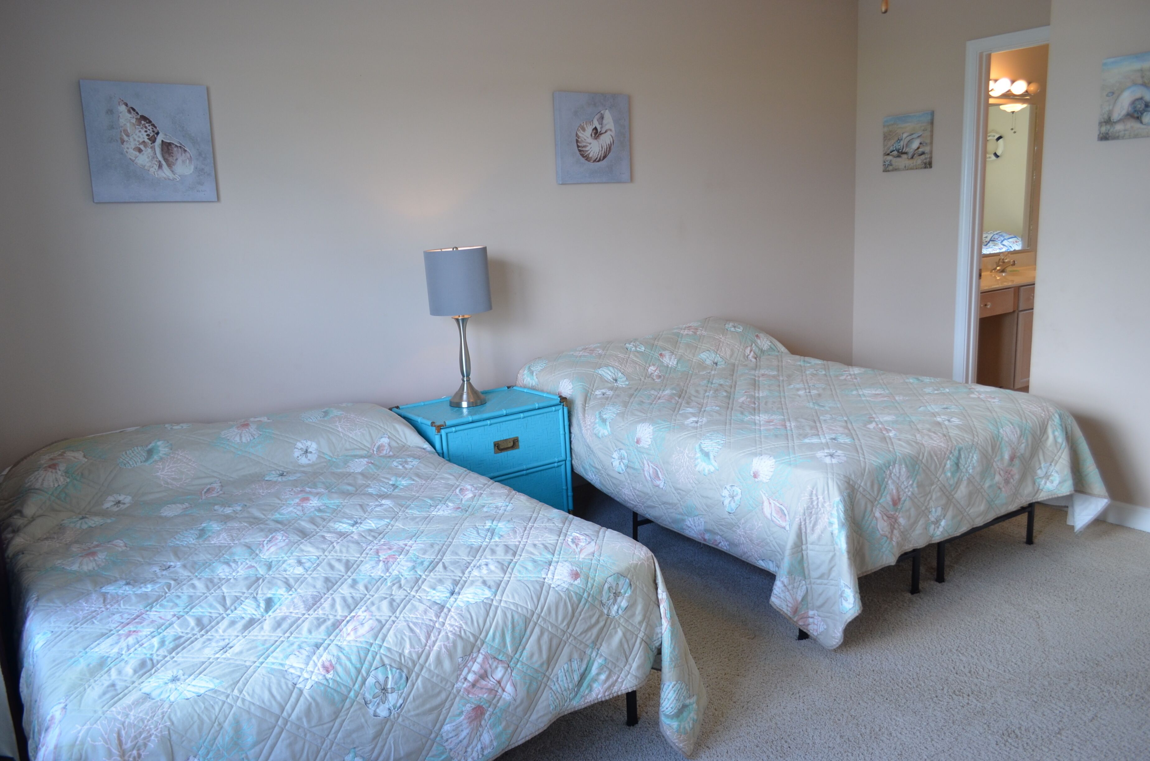 A bedroom with two beds, a nightstand, a lamp, and artwork on the walls.