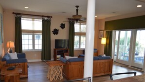 Un salón espacioso con suelo de madera, ventilador de techo, televisor y balcón con vistas.
