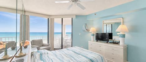 A bedroom with a bed, a TV, a dresser, and a balcony with a view of the ocean.