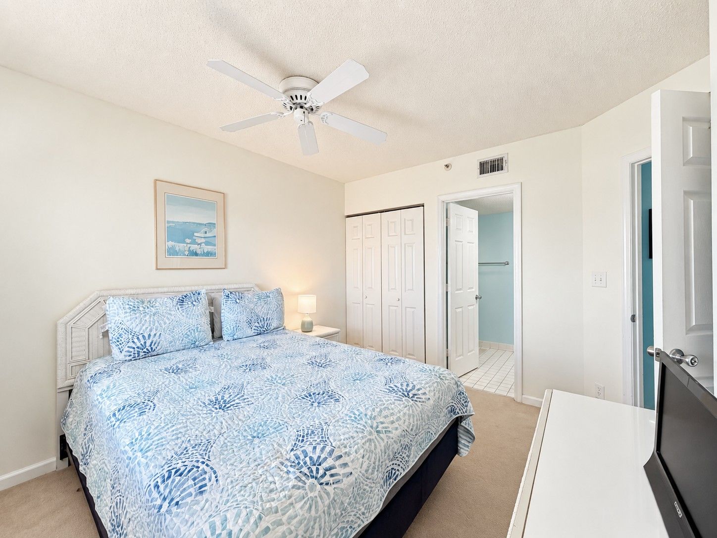 A bedroom with a bed, a ceiling fan, a nightstand, a bedside lamp, and a door leading to a bathroom.