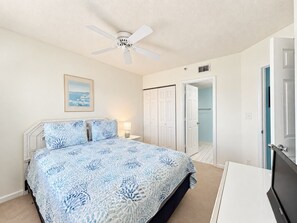 A bedroom with a bed, a ceiling fan, a nightstand, a bedside lamp, and a door leading to a bathroom.