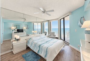 A bedroom with a large bed, a ceiling fan, a TV, and a view of the ocean.