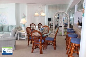 A dining area with wooden chairs and a glass table, a white sofa, and a lamp. - One Ocean Place 505 - Oceanfront in Garden City Beach (Garden City)