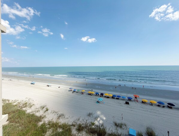 A beach with umbrellas and people, a clear sky, and the ocean.