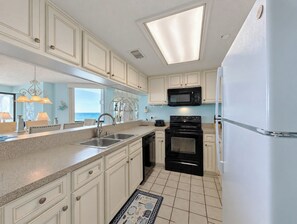 A kitchen with white cabinets, a black stove, a microwave, and a refrigerator.