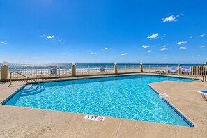 A clear blue pool with a 3 FT no diving sign, a white fence, and a view of the beach.