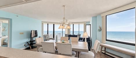 A spacious living area with a dining table, chairs, and a large window overlooking the ocean.