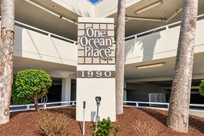 A building entrance with a sign reading 'One Ocean Place 1990' and a parking garage in the background.