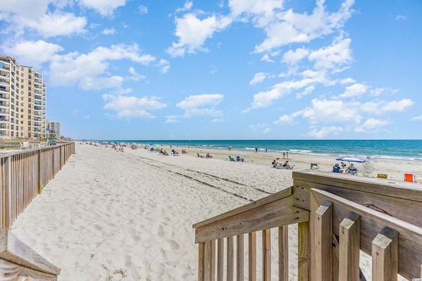 A beach with a wooden boardwalk, sandy beach, and a building in the background. - Mariner's Watch 204 - Oceanfront in Garden City Beach (Garden City)