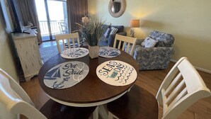 A dining area with a round table, white chairs, and placemats with nautical designs. - Mariner's Watch 204 - Oceanfront in Garden City Beach (Garden City)