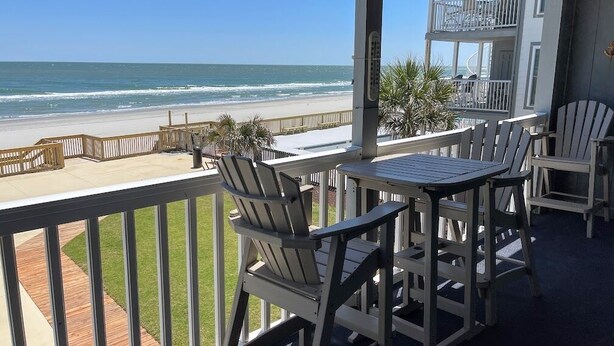 A balcony with Adirondack chairs and a table overlooking a beach. - Mariner's Watch 204 - Oceanfront in Garden City Beach (Garden City)