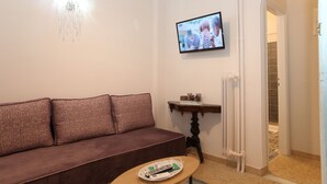 Una sala de estar con un sofá marr ón, una mesita con una bandeja, un televisor montado en la pared y una araña.