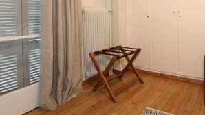 Una habitación con radiador, un tendedero de madera, una ventana con persianas y una puerta con manija.