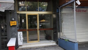 Un escaparate con puerta de vidrio, un banco afuera y una maceta azul con plantas.