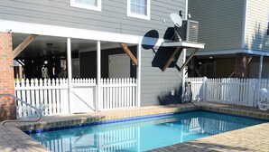 Una piscina con cerca de piquetes blancos, un porche cubierto y una antena parabólica.
