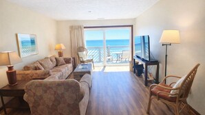 Ein Hotelzimmer mit einer Couch, Sesseln, einem Fernseher und Blick auf den Ozean.