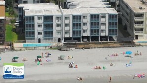 A beachfront hotel with multiple floors, a swimming pool, and beachgoers. - Sea Oaks 304 - Oceanfront in Garden City Beach (Garden City)