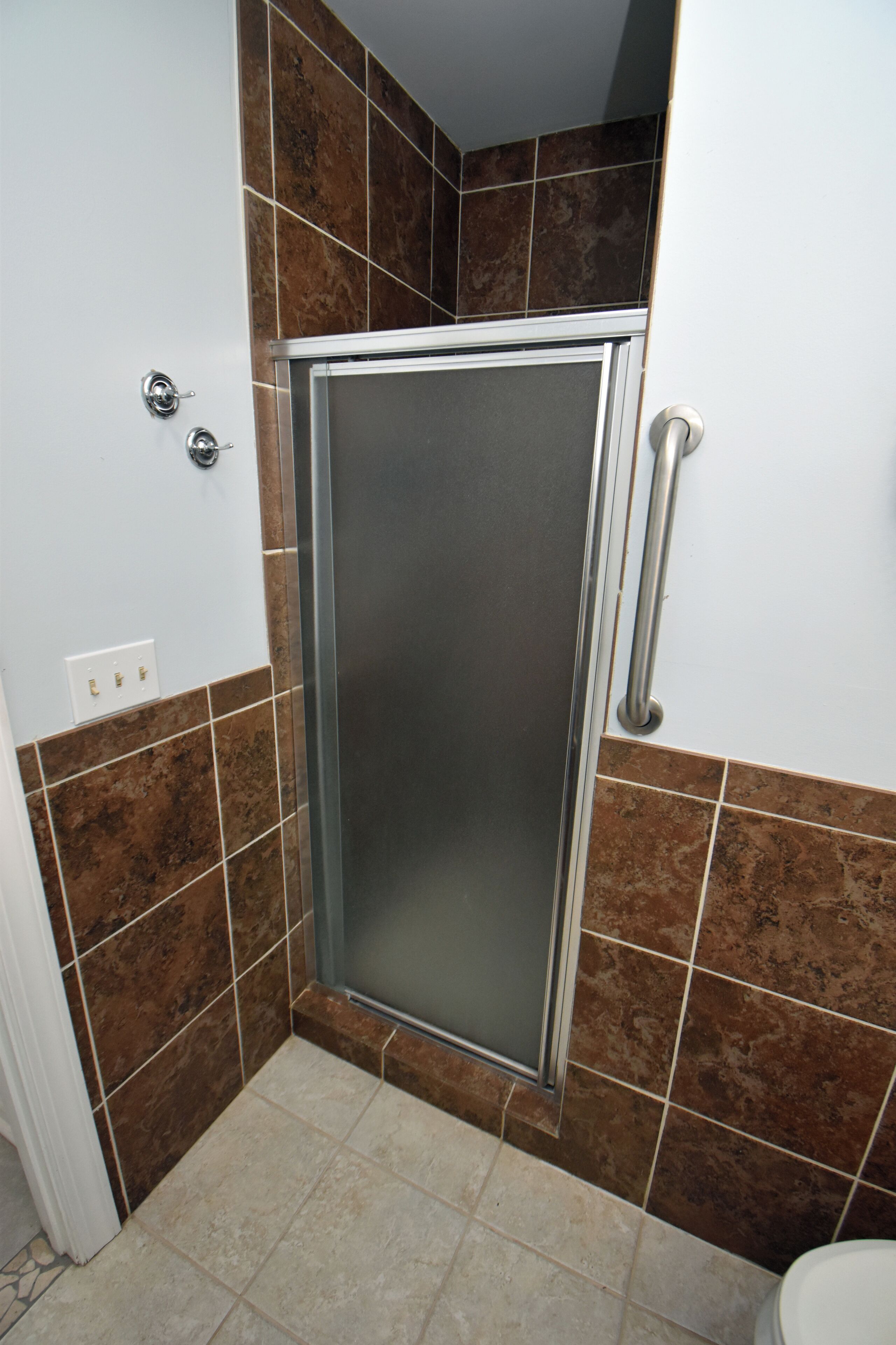 Un baño con cabina de ducha, paredes con azulejos y un inodoro.