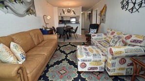 A living room with a brown leather sofa, patterned ottoman, and a decorative rug. - Sea Oaks 304 - Oceanfront in Garden City Beach (Garden City)