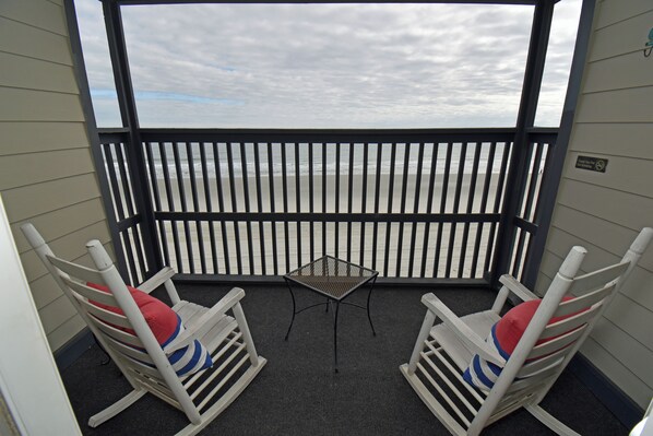 A balcony with two rocking chairs, a small table, and a view of the ocean.