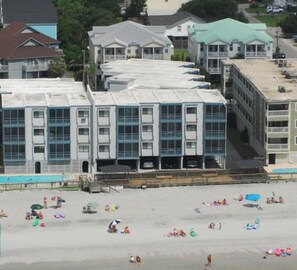 A beachfront hotel with multiple floors, a swimming pool, and beachgoers.