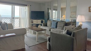 Ein Wohnzimmer mit einer Couch, Sesseln, einem Couchtisch, einem Fernseher und einem Balkon mit Blick.