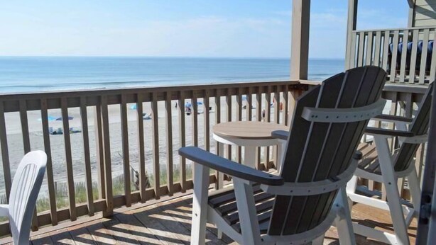 Een houten terras met Adirondack-stoelen met uitzicht op het strand.