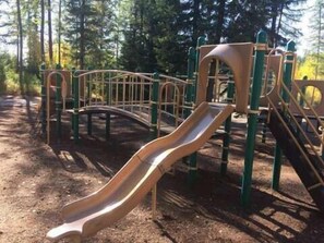 Explore a playground with a curved slide and climbing elements amidst a serene wooded area.