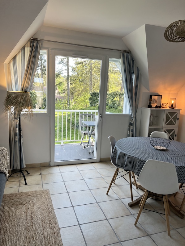 A room with a dining table, chairs, a sofa, a lamp, and a view of the outdoors through a sliding glass door. - Charming duplex and charming residence in Hardelot ideally located (Neufchâtel-Hardelot)