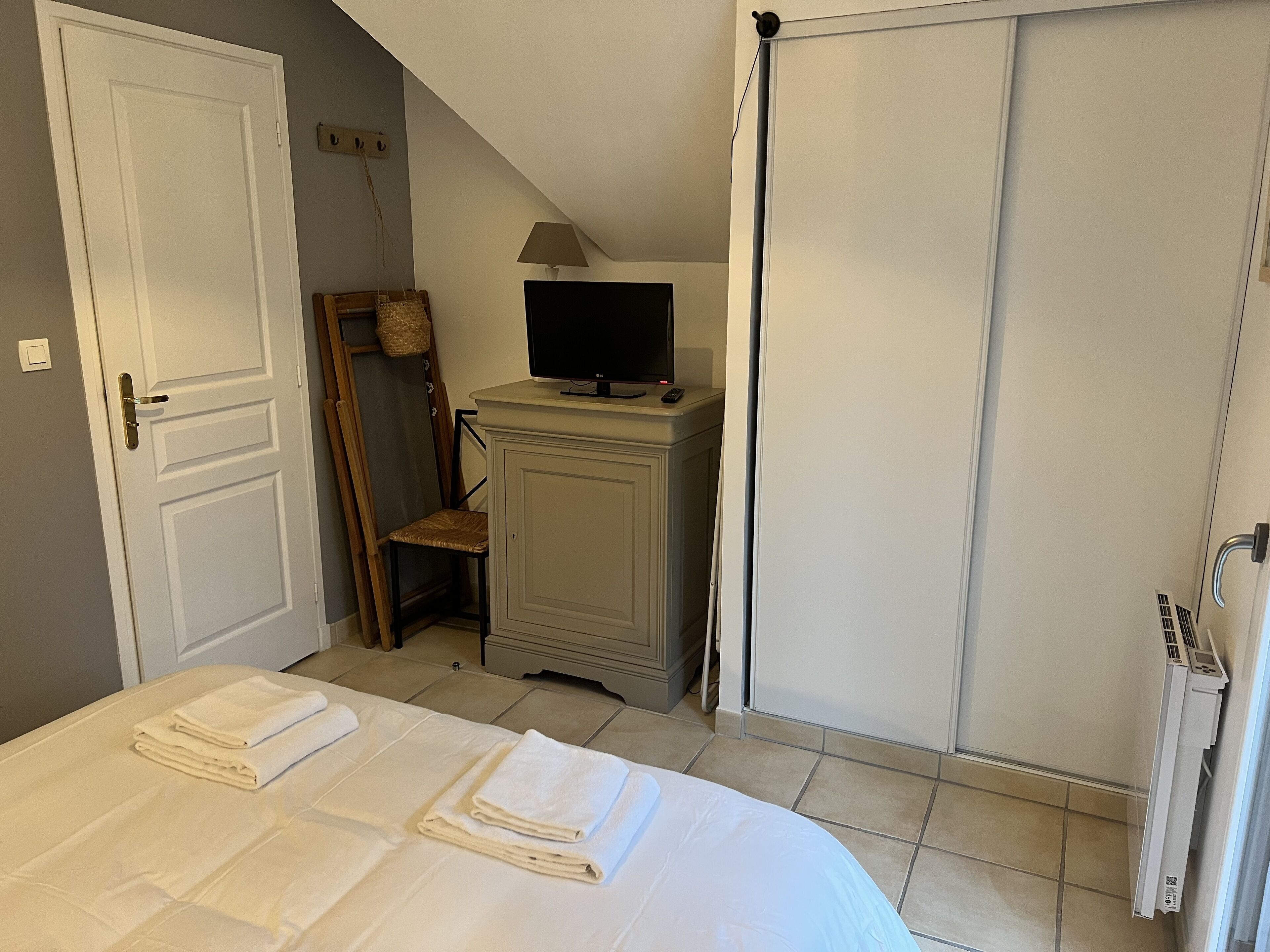 A bedroom with a bed, a TV on a stand, a chair, a wardrobe, and a radiator.