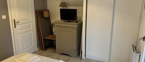 A bedroom with a bed, a TV on a stand, a chair, a wardrobe, and a radiator.