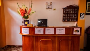 Taulell de recepció d'hotel amb un portàtil, un ram de flors i indicadors dels tipus de habitació i serveis.