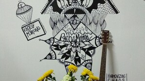 Eine Wand mit einem großen schwarz-weißen Wandgemälde, einer Gitarre und einer Blumenvase.