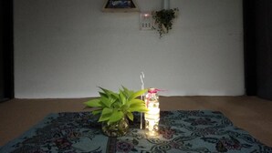Ein Zimmer mit einem gemusterten Teppich, einem Blumentopf und einem beleuchteten Kerzenständer auf dem Boden.