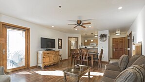 A spacious living area with a wooden floor, a dining table with chairs, a sofa, a television, and a ceiling fan. - Some of the best direct ski access on the mountain!! 2 bedroom with beautiful valley views!! (Whitefish)