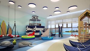 A children's play area with a slide, swings, and a view of the sea through large windows. - Scenia Bay Residences (Bac Nha Trang)