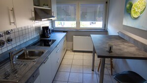 A modern kitchen with white cabinets, a built-in dishwasher, and a window with blinds. - FeWo Studenik (Neuried)