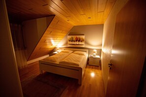 A bedroom with a sloped ceiling, a bed with white bedding, two bedside tables with lamps, and a wall-mounted artwork of trees. - FeWo Studenik (Neuried)